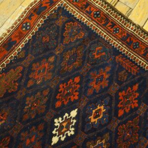 Dark blue rug with rust and cream geometric motifs and a detailed border rests on distressed light wood floor.