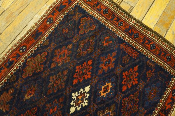 Dark blue rug with rust and cream geometric motifs and a detailed border rests on distressed light wood floor.