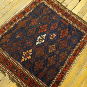 Small navy rug with rust geometric patterns and a detailed border on bright yellow wooden floorboards.