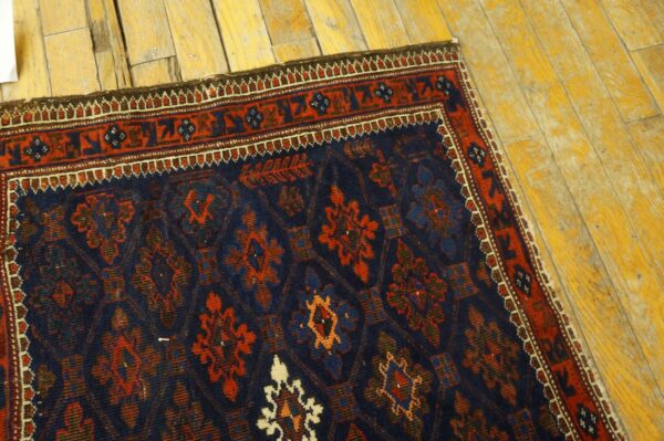 Textured navy rug with a repeating red and blue medallion pattern shown on distressed yellow hardwood.