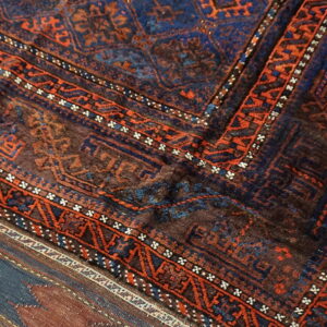 Dark rug corner with detailed geometric patterns in brown, navy, and bright orange on rustic wood planks.