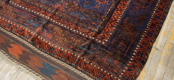 Dark rug corner with detailed geometric patterns in brown, navy, and bright orange on rustic wood planks.