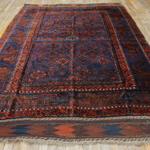 A dark blue and rust-red geometric patterned rug with low pile rests on distressed wooden floorboards.