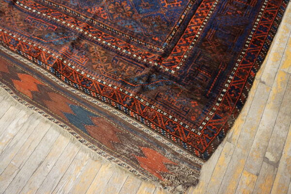 High-pile blue and rust geometric rug meets a flat-woven border on distressed light wood flooring.