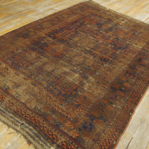Distressed geometric rug featuring rust, navy, and brown patterns rests on light, visibly worn wooden floorboards.