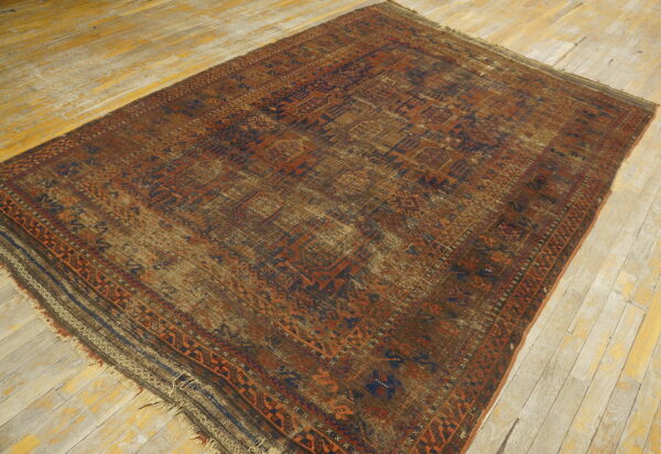 A worn low-pile rug with geometric patterns in rust, brown, and navy rests on light wood floors.