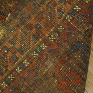 Folded dark brown rug featuring tightly woven red and blue geometric patterns on light wooden flooring.