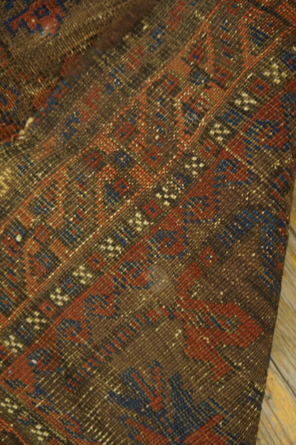 Folded dark brown rug featuring tightly woven red and blue geometric patterns on light wooden flooring.