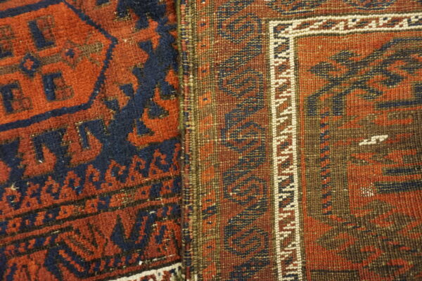 Detail shot of two adjacent rugs, showing dense pile red/blue pattern next to a flatweave brown border.