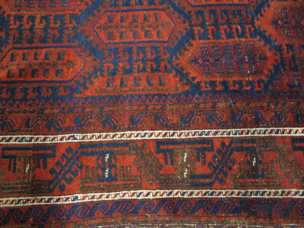 Red and navy geometric rug with detailed tribal motifs, striped borders, and a visibly low pile texture.