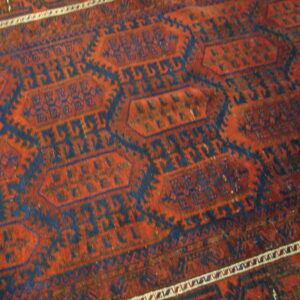 Close-up of a rug featuring rust red and navy blue geometric octagonal patterns and a white striped border.