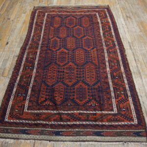 Red-orange rug with dark blue geometric medallions and borders on worn, light wood planks.