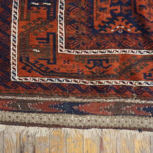 Rust and navy tribal rug with angular patterns and fringe rests on weathered light wood flooring.