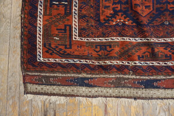 Rust and navy tribal rug with angular patterns and fringe rests on weathered light wood flooring.