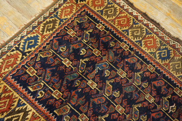 Geometric tribal rug in deep navy, red, gold, and brown colors rests on weathered light wood plank flooring.