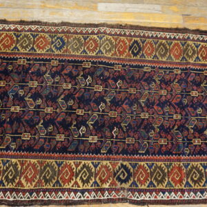 Geometric dark blue rug with red and gold motifs lays flat on light-colored wood flooring.