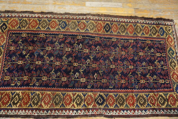 Geometric dark blue rug with red and gold motifs lays flat on light-colored wood flooring.