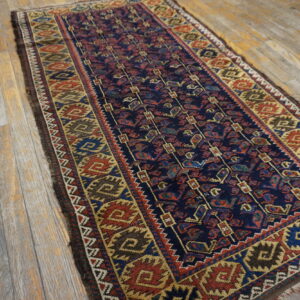 A traditional runner rug with a navy blue field and red, gold, and brown geometric patterns rests on weathered wood planks.