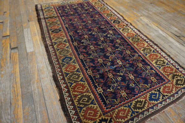A traditional runner rug with a navy blue field and red, gold, and brown geometric patterns rests on weathered wood planks.