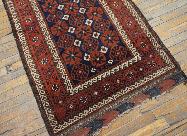 Low-pile geometric rug in navy and rust red with detailed borders on light wood flooring.