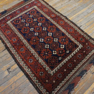 Red and navy geometric rug with detailed borders lying on distressed gray wood plank flooring.