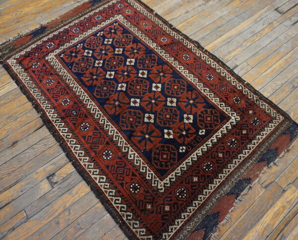 Red and navy geometric rug with detailed borders lying on distressed gray wood plank flooring.