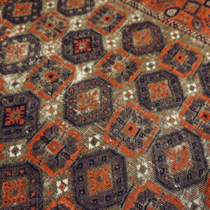 Close-up geometric rug detail featuring repeating medallions in dark brown, rust orange, navy, and faded tan.