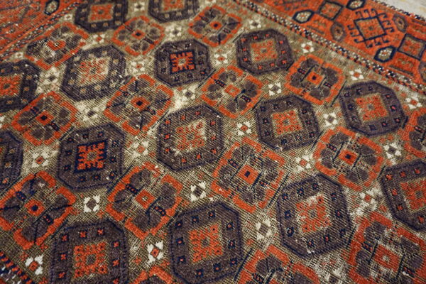Close-up geometric rug detail featuring repeating medallions in dark brown, rust orange, navy, and faded tan.