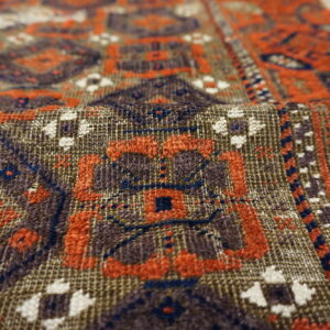 Detailed view of a woven rug folded, featuring geometric patterns in brown, rust, blue, and cream.
