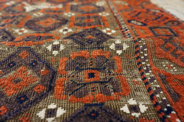 Detailed view of a woven rug folded, featuring geometric patterns in brown, rust, blue, and cream.
