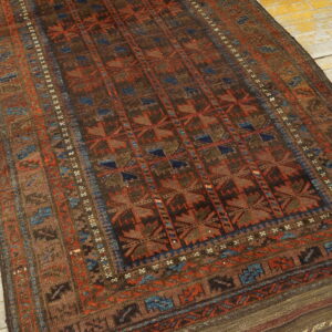 Brown, rust, and blue patterned rug with low pile lying on distressed yellow wood floorboards.