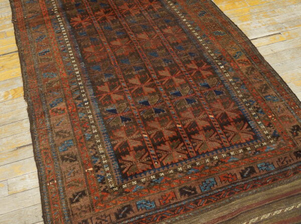 Brown, rust, and blue patterned rug with low pile lying on distressed yellow wood floorboards.