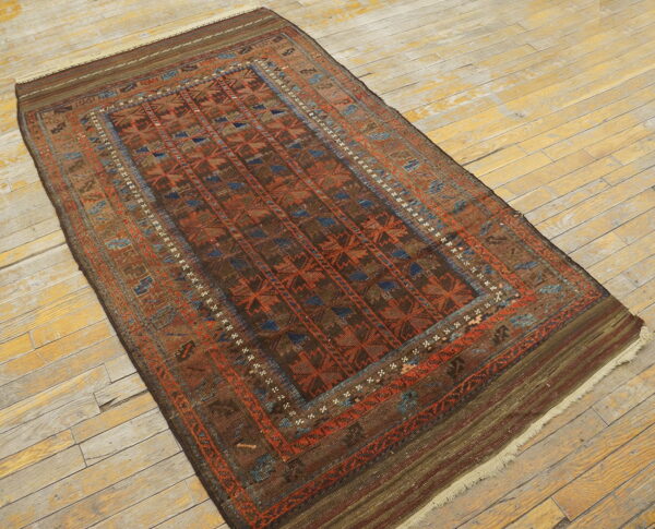 A brown and rust geometric tribal rug with blue accents rests on distressed yellow wood floors.