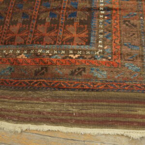 Close-up of a brown, rust, and blue patterned rug with a striped flatweave end showing fringe on wood planks.