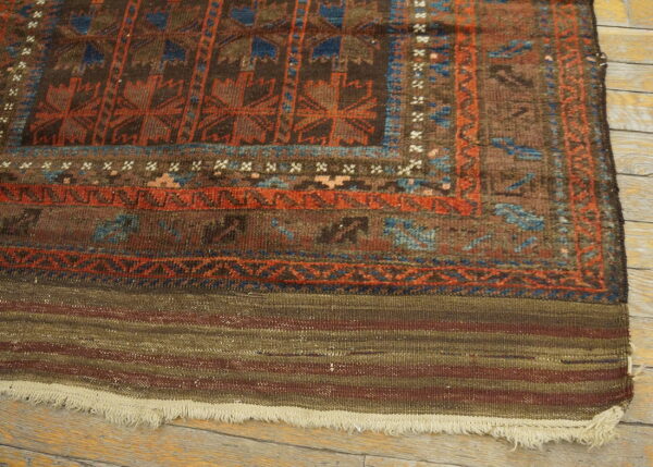 Close-up of a brown, rust, and blue patterned rug with a striped flatweave end showing fringe on wood planks.