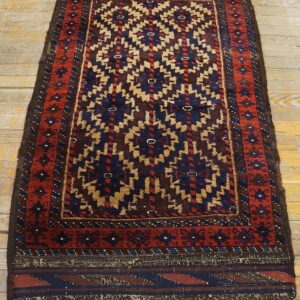 Small rug with red, navy, and tan geometric patterns displayed on rustic wooden flooring.