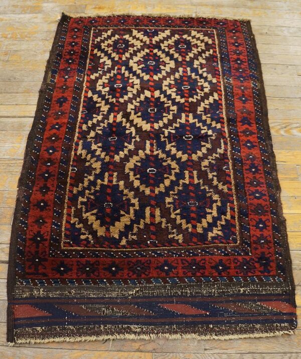 Small rug with red, navy, and tan geometric patterns displayed on rustic wooden flooring.