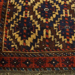 Thick pile rug detail featuring traditional geometric patterns in navy, rust, tan, and brown over wood.