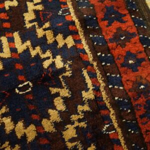 High-pile rug with geometric gold, navy, red, and brown patterns rests on light wood planks.