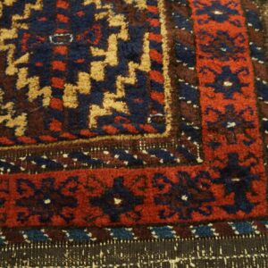 Geometric red, navy, and tan high-pile rug detail with detailed borders shown on light wood flooring.