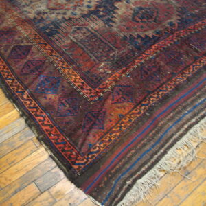 Distressed geometric rug in maroon and navy with fringe rests on light wood plank flooring.