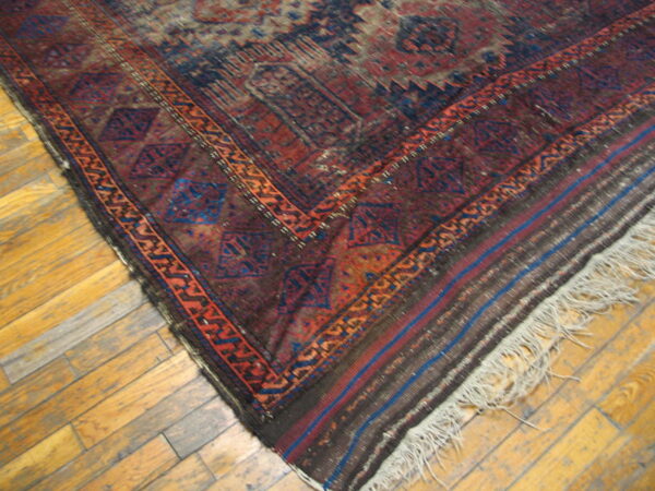 Distressed geometric rug in maroon and navy with fringe rests on light wood plank flooring.