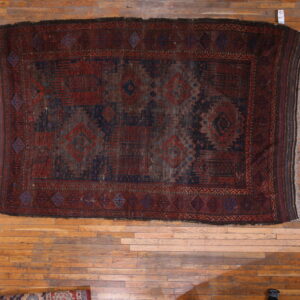 Distressed tribal rug in dark red and indigo blue with geometric motifs on light wood flooring.