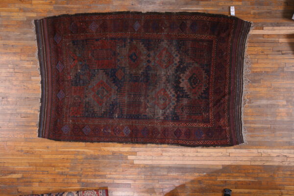 Distressed tribal rug in dark red and indigo blue with geometric motifs on light wood flooring.
