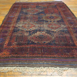 Worn traditional rug in deep red and navy blue geometric patterns on light hardwood.