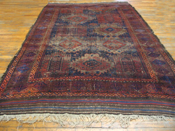 Worn traditional rug in deep red and navy blue geometric patterns on light hardwood.
