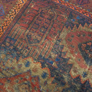 The rug displays a distressed geometric design in red, navy blue, brown, and a narrow orange border.