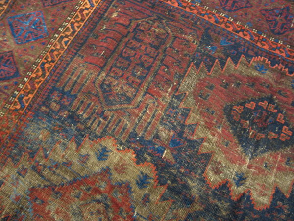The rug displays a distressed geometric design in red, navy blue, brown, and a narrow orange border.