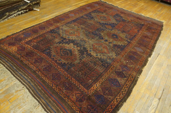 Dark low-pile rug with geometric medallions and intricate borders in red, blue, and brown tones, on hardwood.