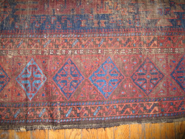 Worn, geometric flatweave rug in red and indigo with diamond motifs visible against wood flooring.